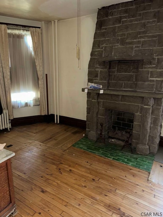 unfurnished living room featuring a stone fireplace, radiator, and hardwood / wood-style floors