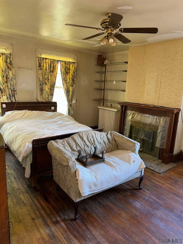 bedroom featuring ceiling fan, dark hardwood / wood-style flooring, and a tiled fireplace