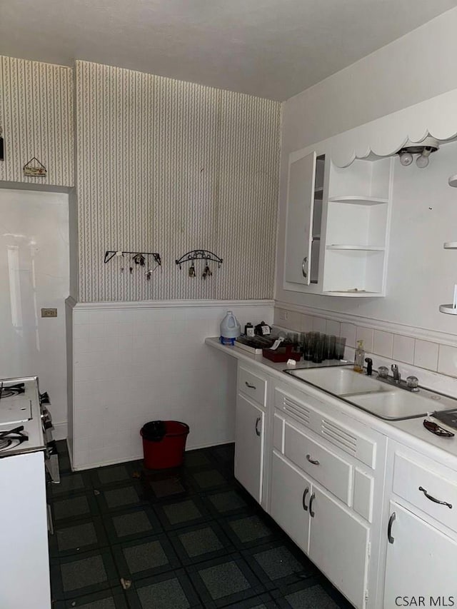 kitchen featuring range, sink, tile walls, and white cabinets