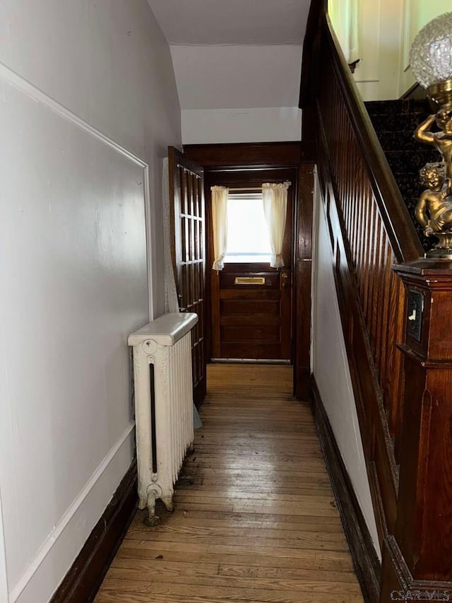 corridor with lofted ceiling, radiator heating unit, and dark hardwood / wood-style floors