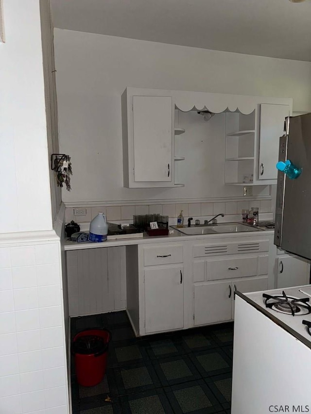 kitchen featuring tasteful backsplash, white cabinetry, white gas range, sink, and fridge