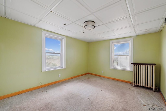 carpeted empty room featuring radiator heating unit, a paneled ceiling, and plenty of natural light