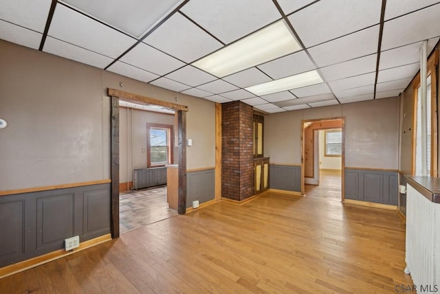 unfurnished living room featuring a paneled ceiling, radiator, light hardwood / wood-style floors, and ornate columns