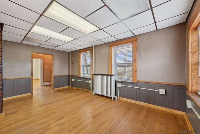 empty room featuring radiator heating unit, light hardwood / wood-style flooring, and a drop ceiling