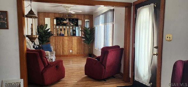 living area featuring ceiling fan, wooden walls, and hardwood / wood-style floors