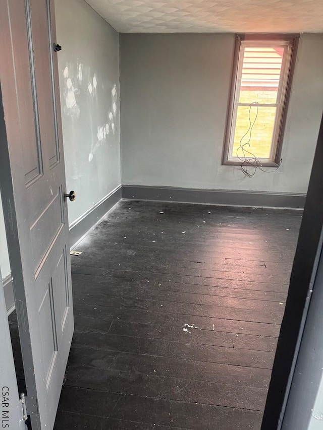 empty room with dark wood-style flooring and baseboards