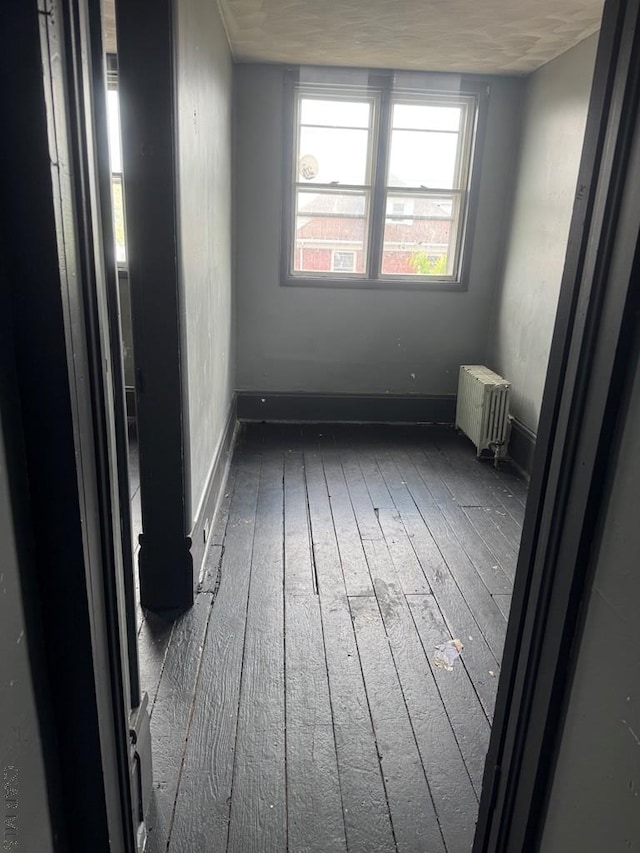 empty room with radiator heating unit, baseboards, and hardwood / wood-style floors