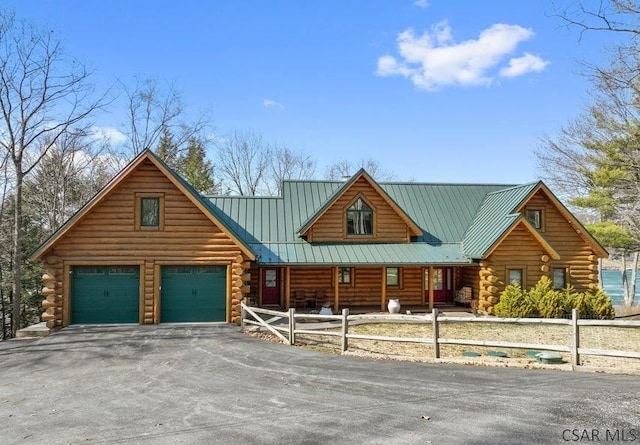 cabin featuring aphalt driveway, a fenced front yard, log siding, metal roof, and an attached garage