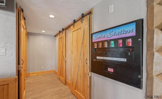 corridor featuring light wood-type flooring, a textured ceiling, recessed lighting, a barn door, and baseboards