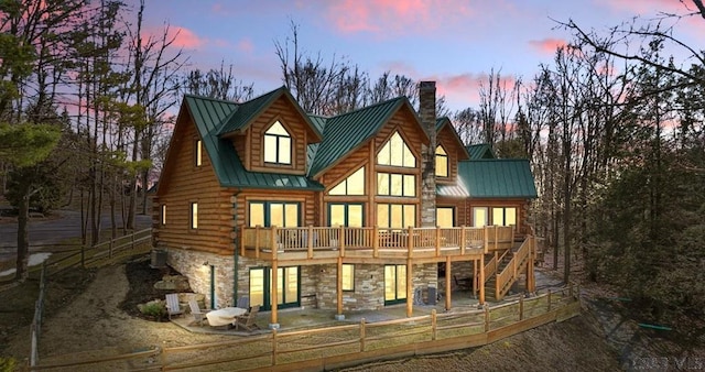 back of house featuring a standing seam roof, a deck, a chimney, and metal roof