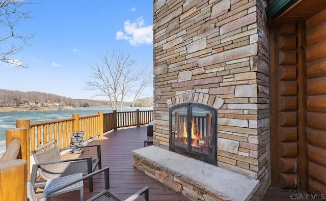 wooden terrace with a water view and an outdoor stone fireplace