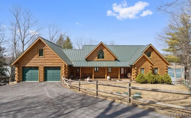 log-style house featuring log siding, covered porch, a fenced front yard, and metal roof