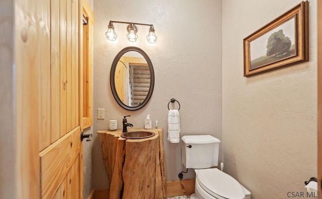 half bath with toilet, vanity, and a textured wall