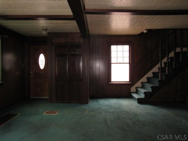 carpeted foyer entrance with stairway, beam ceiling, visible vents, and wooden walls