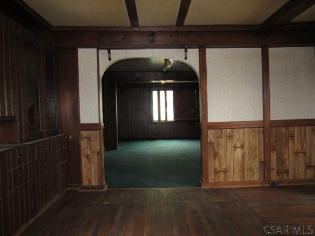 unfurnished room with a wainscoted wall, wooden walls, arched walkways, and dark wood-type flooring