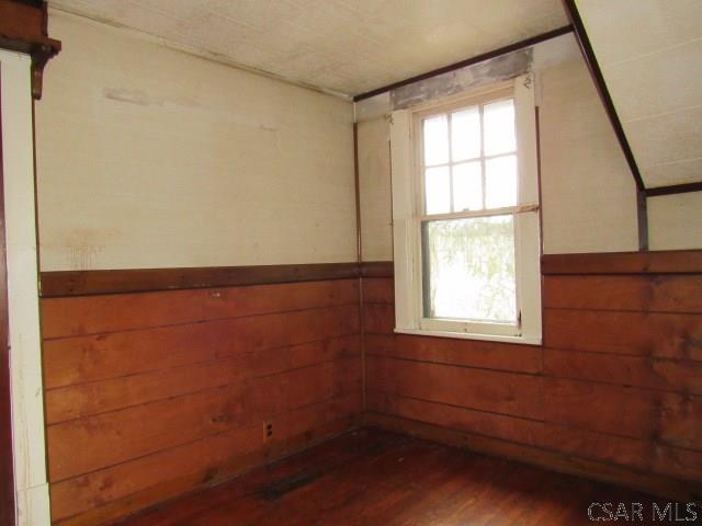 empty room featuring a healthy amount of sunlight, wooden walls, dark wood-style flooring, and wainscoting