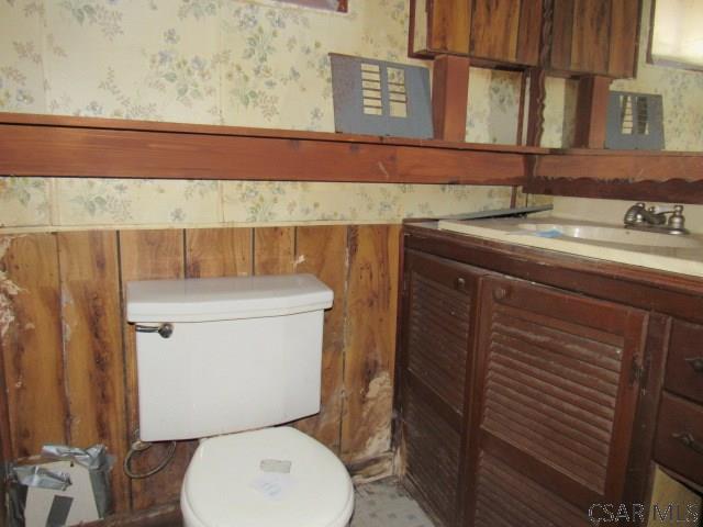 half bath with a wainscoted wall, toilet, vanity, and wallpapered walls