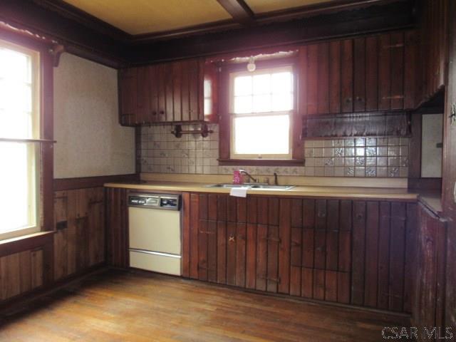 kitchen with white dishwasher, light wood-style flooring, a sink, light countertops, and wainscoting