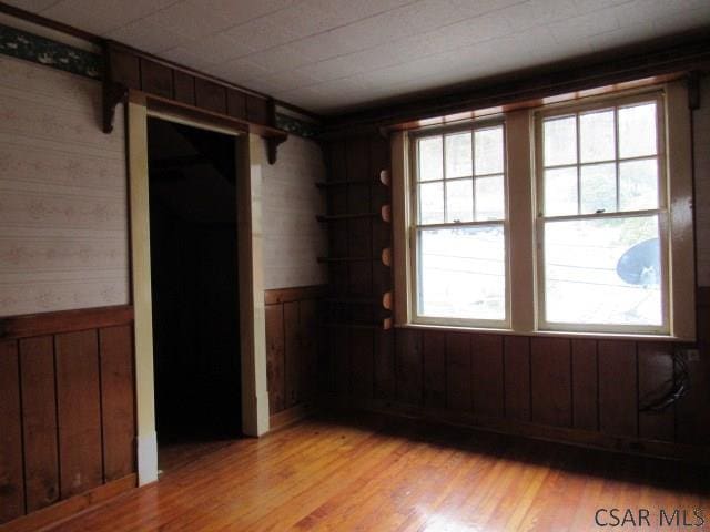 unfurnished room with light wood finished floors, wood walls, and wainscoting