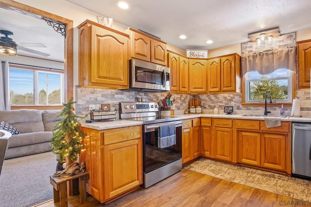 kitchen with stainless steel appliances, a sink, light countertops, light wood finished floors, and tasteful backsplash