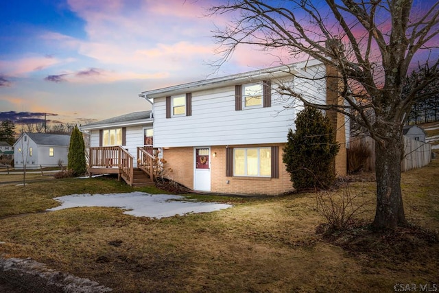 view of front of home featuring brick siding, fence, a wooden deck, and a lawn