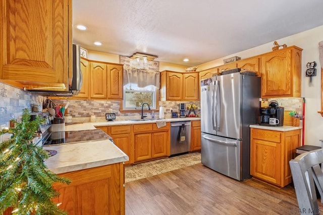 kitchen featuring a sink, light wood-style floors, light countertops, appliances with stainless steel finishes, and decorative backsplash