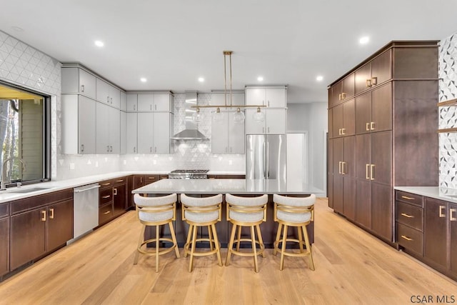 kitchen with wall chimney exhaust hood, sink, a center island, stainless steel appliances, and light hardwood / wood-style floors