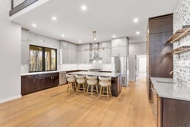 kitchen with sink, light hardwood / wood-style flooring, appliances with stainless steel finishes, a kitchen breakfast bar, and decorative light fixtures