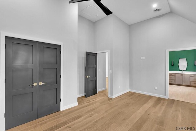 unfurnished bedroom featuring light hardwood / wood-style flooring, ceiling fan, high vaulted ceiling, ensuite bathroom, and a closet