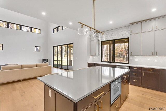 kitchen with a center island, hanging light fixtures, light wood-type flooring, stainless steel microwave, and decorative backsplash