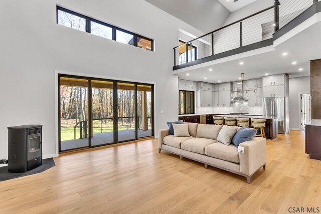 living room featuring a high ceiling, a wood stove, and light hardwood / wood-style flooring