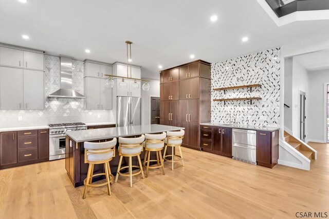 kitchen with stainless steel appliances, light hardwood / wood-style flooring, a breakfast bar area, and wall chimney exhaust hood