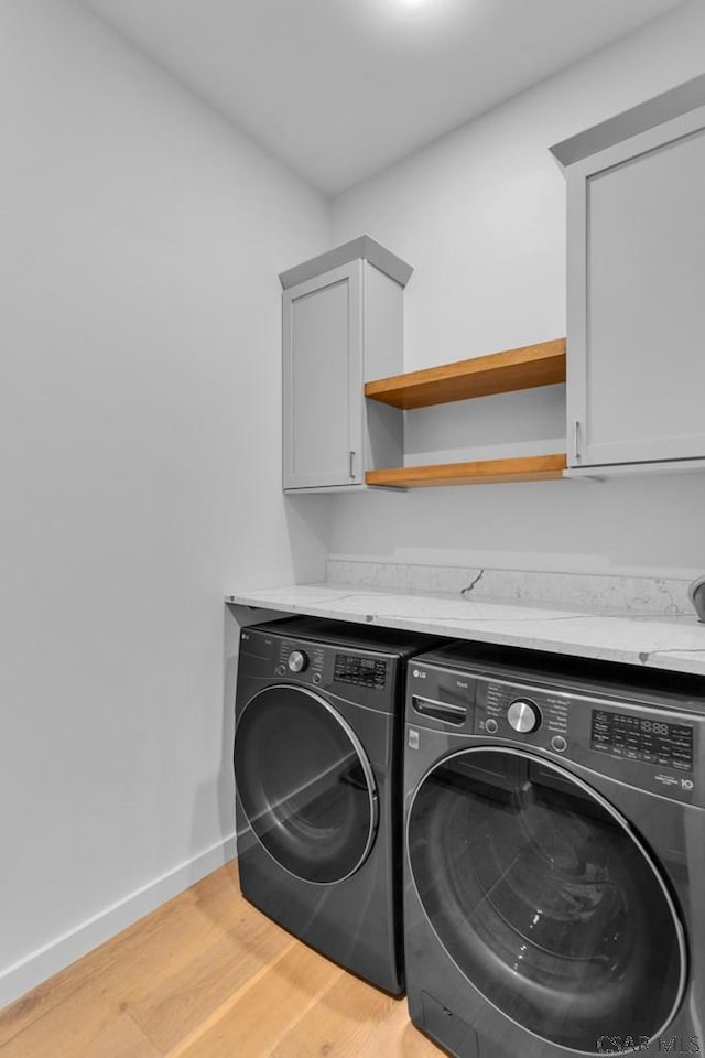 laundry area featuring cabinets, light wood-type flooring, and washer and clothes dryer