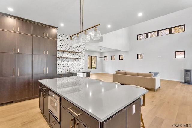 kitchen with a kitchen island, appliances with stainless steel finishes, decorative light fixtures, dark brown cabinetry, and light hardwood / wood-style floors