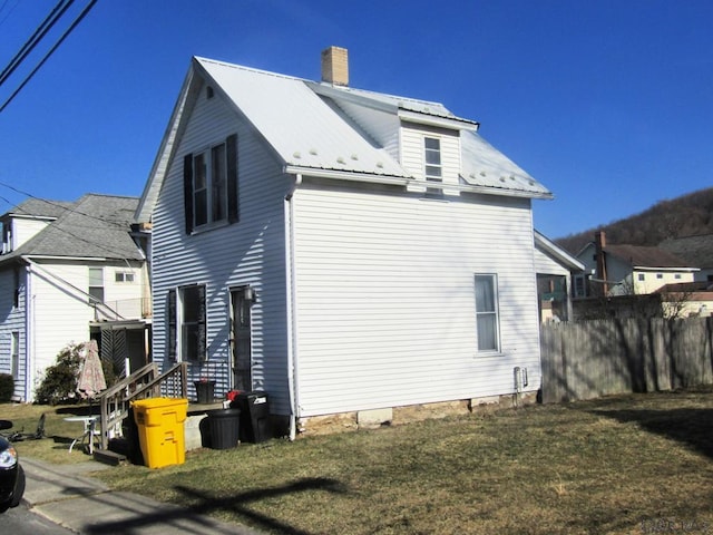 view of home's exterior with metal roof, a yard, a chimney, and fence