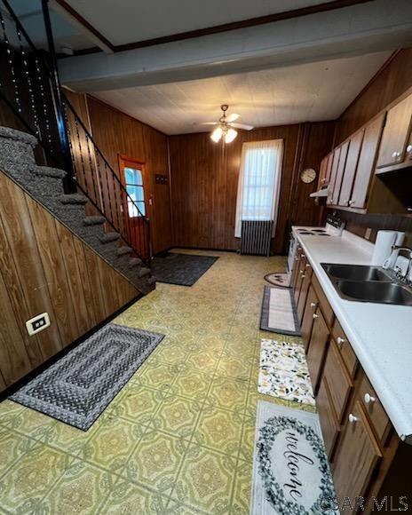 kitchen with ceiling fan, wooden walls, sink, and stove