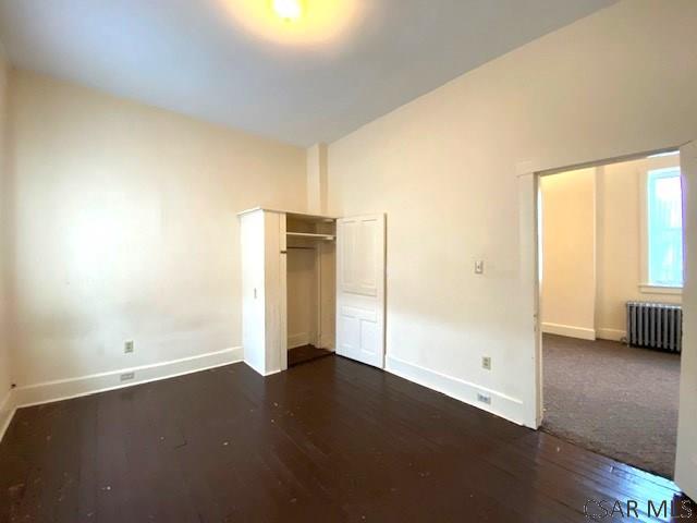 unfurnished bedroom featuring radiator and dark hardwood / wood-style flooring