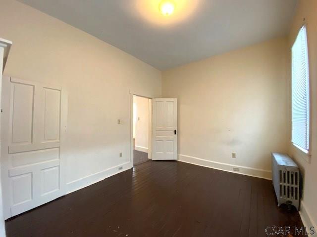 spare room featuring dark wood-type flooring and radiator heating unit