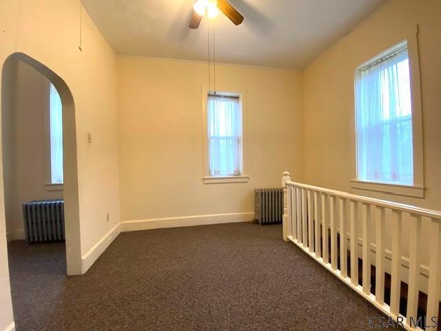 spare room featuring ceiling fan, radiator heating unit, and dark colored carpet