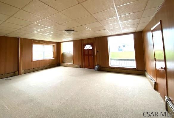 carpeted empty room featuring a paneled ceiling, baseboard heating, and wood walls