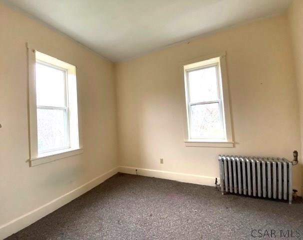 carpeted empty room featuring radiator and a wealth of natural light