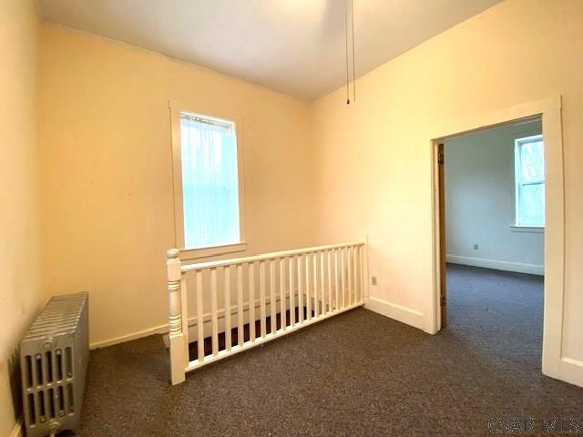 empty room featuring radiator and dark colored carpet