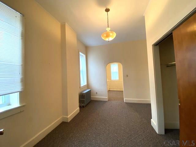 unfurnished bedroom featuring multiple windows, radiator heating unit, a closet, and dark colored carpet