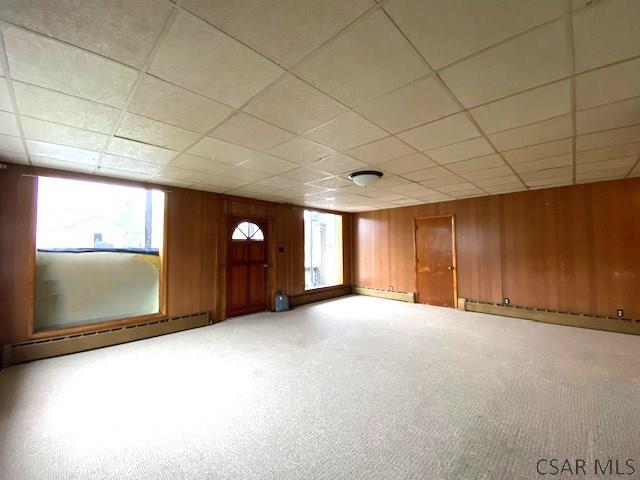 basement with a healthy amount of sunlight, wooden walls, a drop ceiling, and baseboard heating