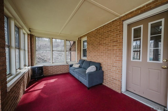 sunroom with outdoor lounge area, carpet flooring, a wood stove, and brick wall