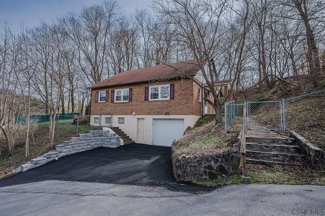 view of front of home featuring driveway, a gate, stairway, brick siding, and a garage