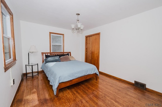bedroom with a closet, visible vents, a chandelier, baseboards, and wood finished floors
