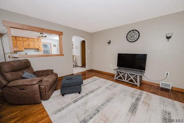 living area with arched walkways, baseboards, visible vents, and wood finished floors