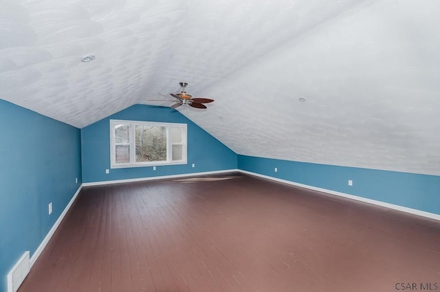 bonus room featuring a textured ceiling, visible vents, baseboards, hardwood / wood-style floors, and vaulted ceiling