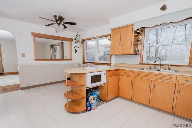 kitchen featuring light countertops, a sink, white microwave, and open shelves